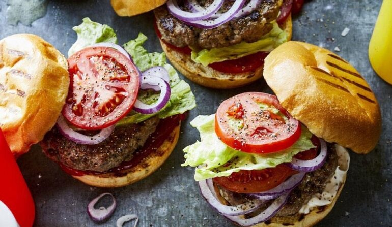 Grilled burgers stacked with tomato, onion and lettuce on a serving board