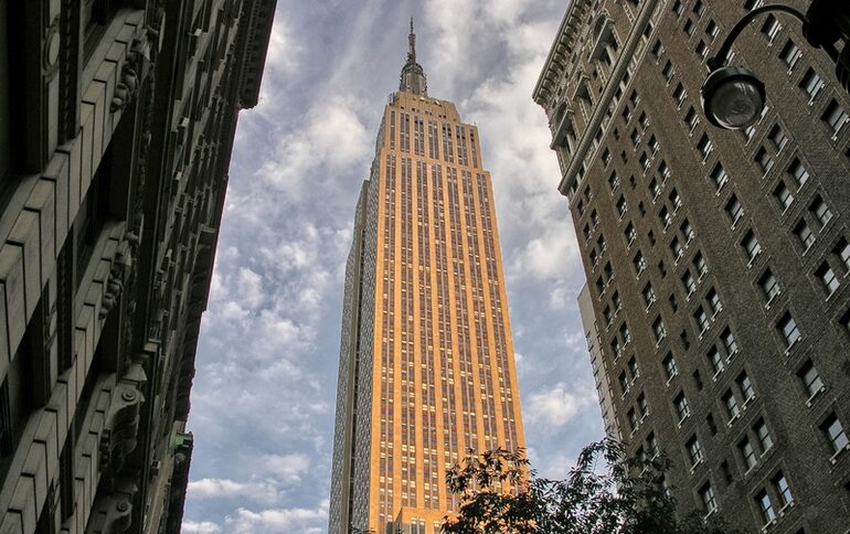 A sunlit skyscraper towering between older city buildings
